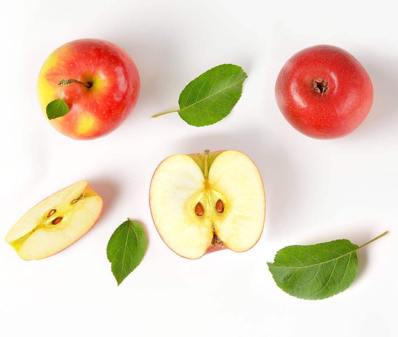 Zwei ganze rote Äpfel und ein aufgeschnittener Apfel mit Kernen, umgeben von grünen Blättern auf einem weißen Hintergrund.
