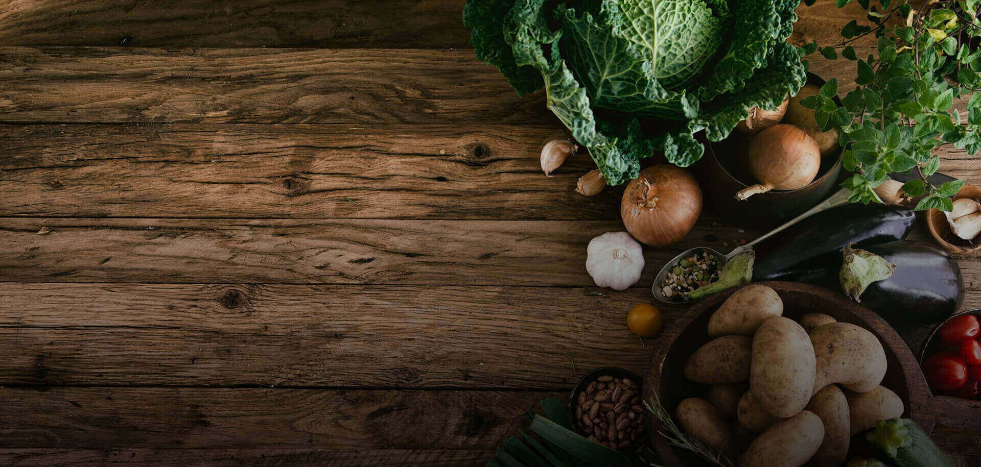 Ein rustikaler Holztisch, geschmückt mit frischem Gemüse wie Kohl, Zwiebeln, Knoblauch, Kartoffeln und Kräutern, schafft eine lebendige Ernteszene.