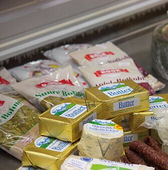 Eine Vielzahl von Lebensmitteln, darunter Butter, Gewürze und Wurstwaren, die auf einer von Verpackungen umgebenen Arbeitsplatte ausgestellt sind.