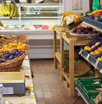 Ein gemütlicher Obstmarkt mit Körben voller Orangen, Pflaumen und Bananen, in denen frische Produkte in Holzregalen präsentiert werden.